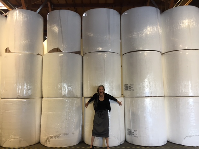 Mary Roach stands in front of giant paper rolls, smiling
