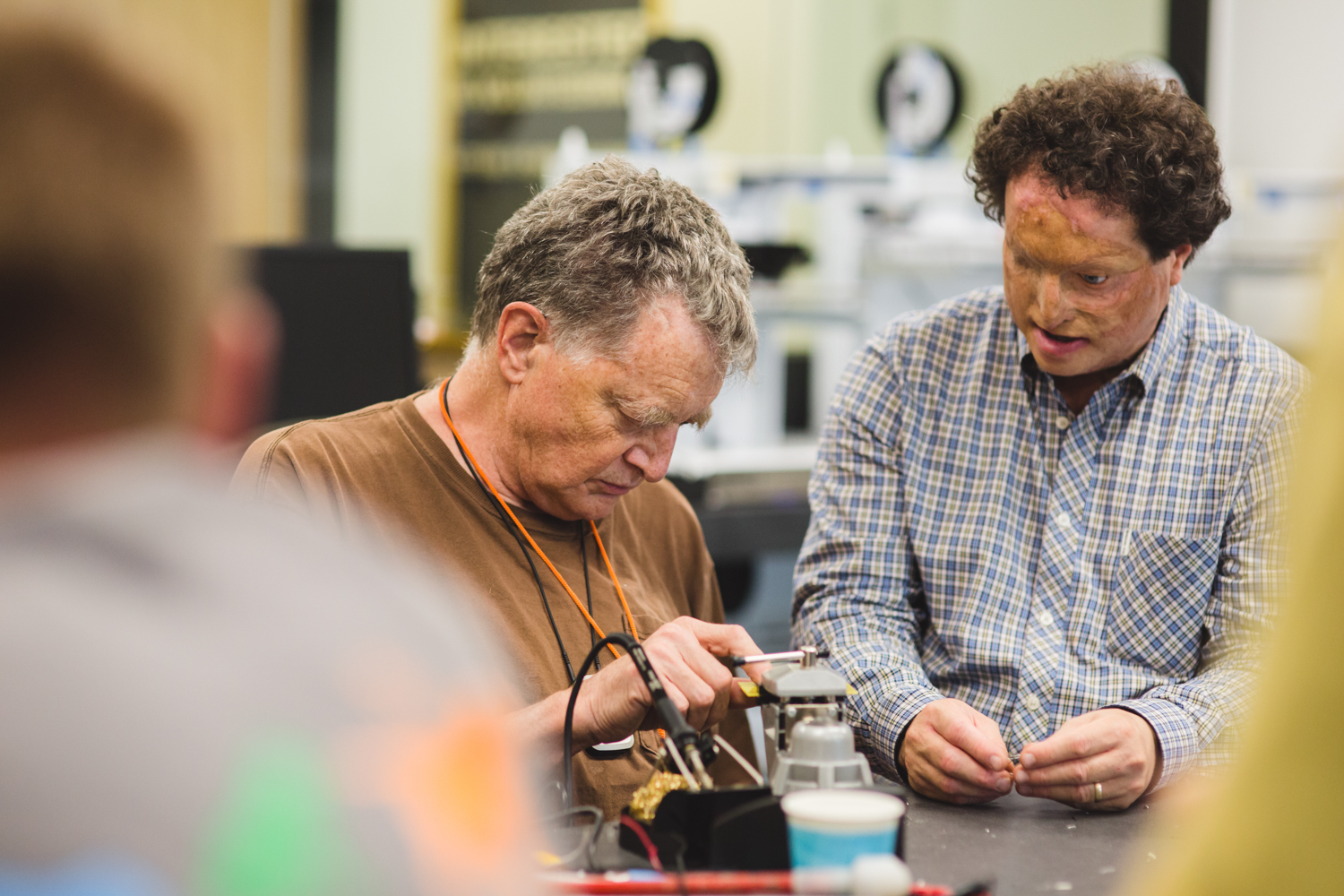 Workshop facilitator Dr. Joshua Miele of the Smith-Kettlewell Rehabilitation Engineering Research Center on Low Vision and Blindness oversees the work of a male soldering student. 