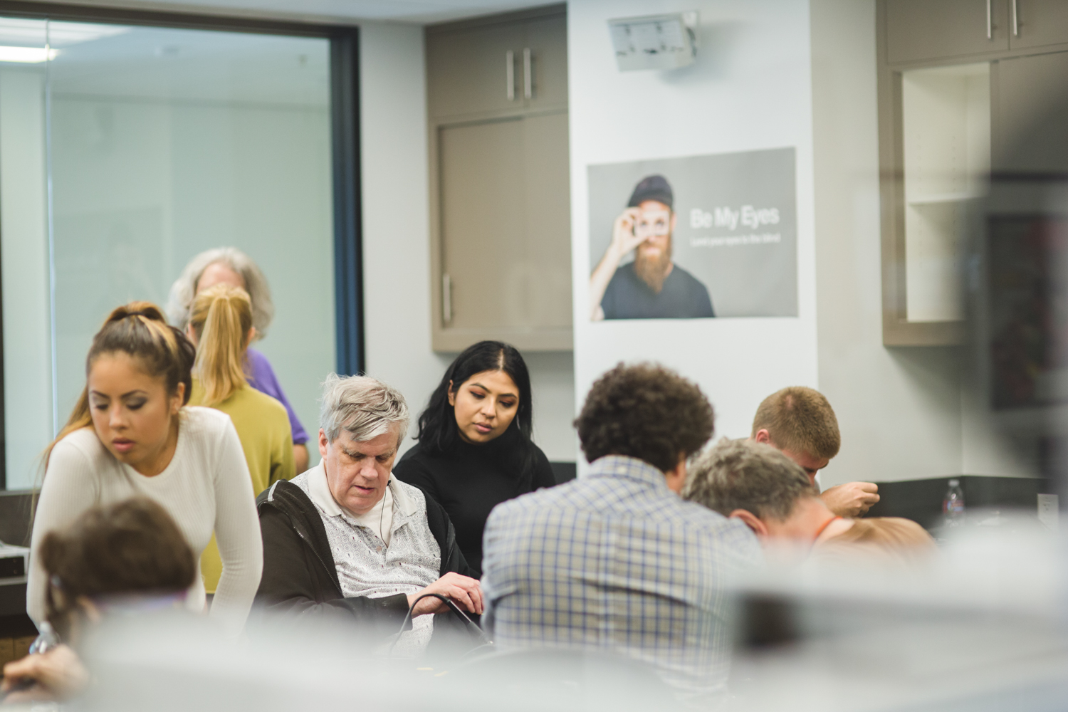 A diverse array of students, instructors, and volunteers are hard at work in the LightHouse’s Innovation Lab. A Be My Eyes poster stands out in the background as an indicator of the space’s many uses. 