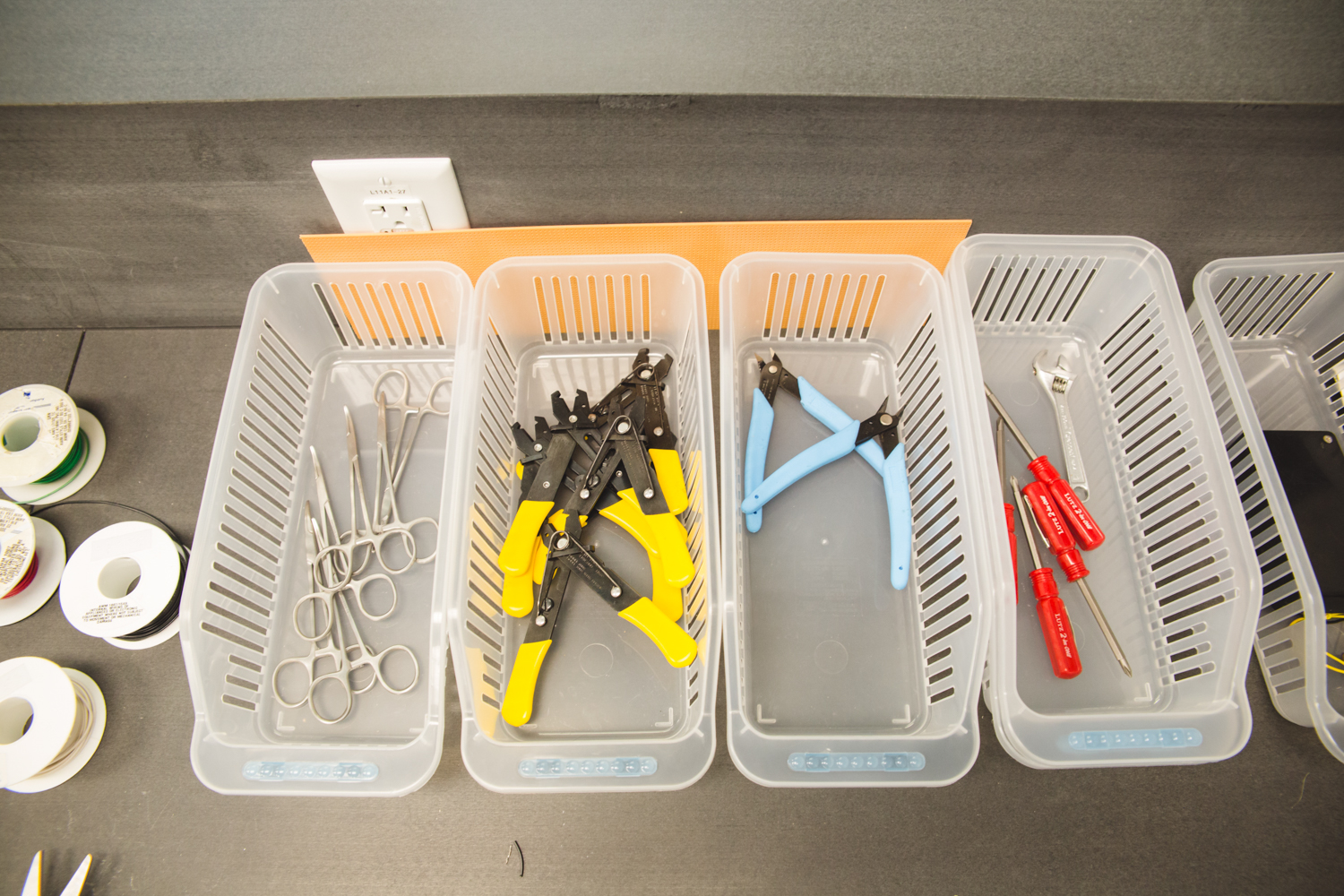 Baskets hold some of the essential components for making continuity testers: stainless steel forceps, insulated handle-wire strippers, wire cutters, wrenches, and Phillips-Head screwdrivers. A few spools of insulated wire — also essential — sit to the left.