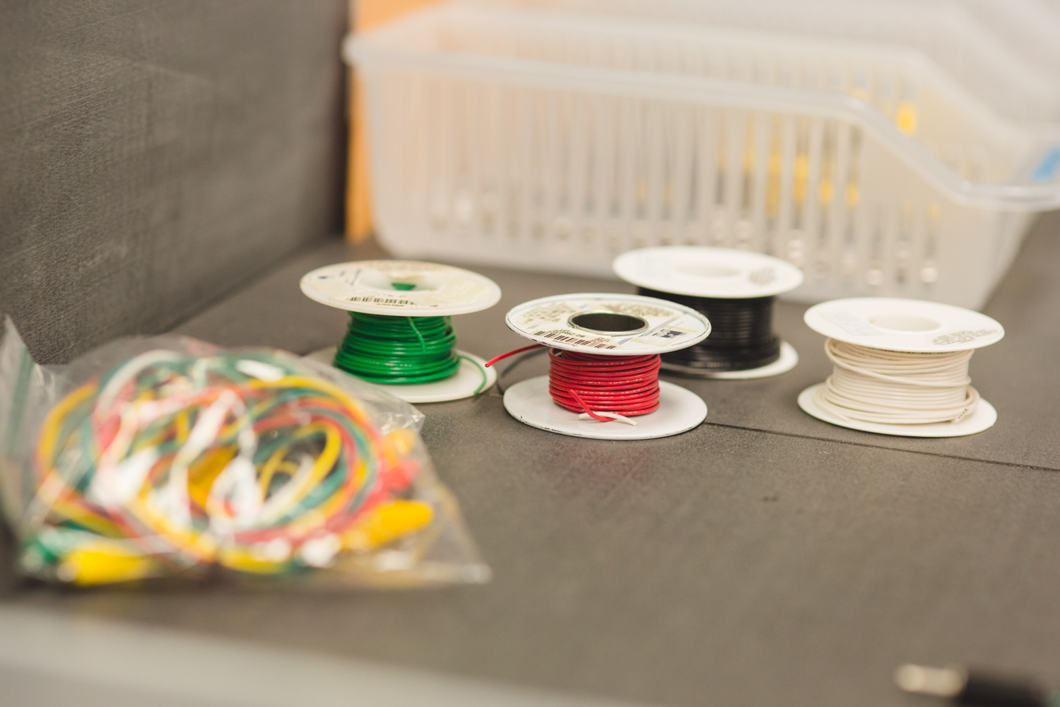 Red, green, black and white insulated wire spools sit on a table. Color indicators help sighted individuals distinguish between wires, while vision impaired students use a system of knots to differentiate between them.