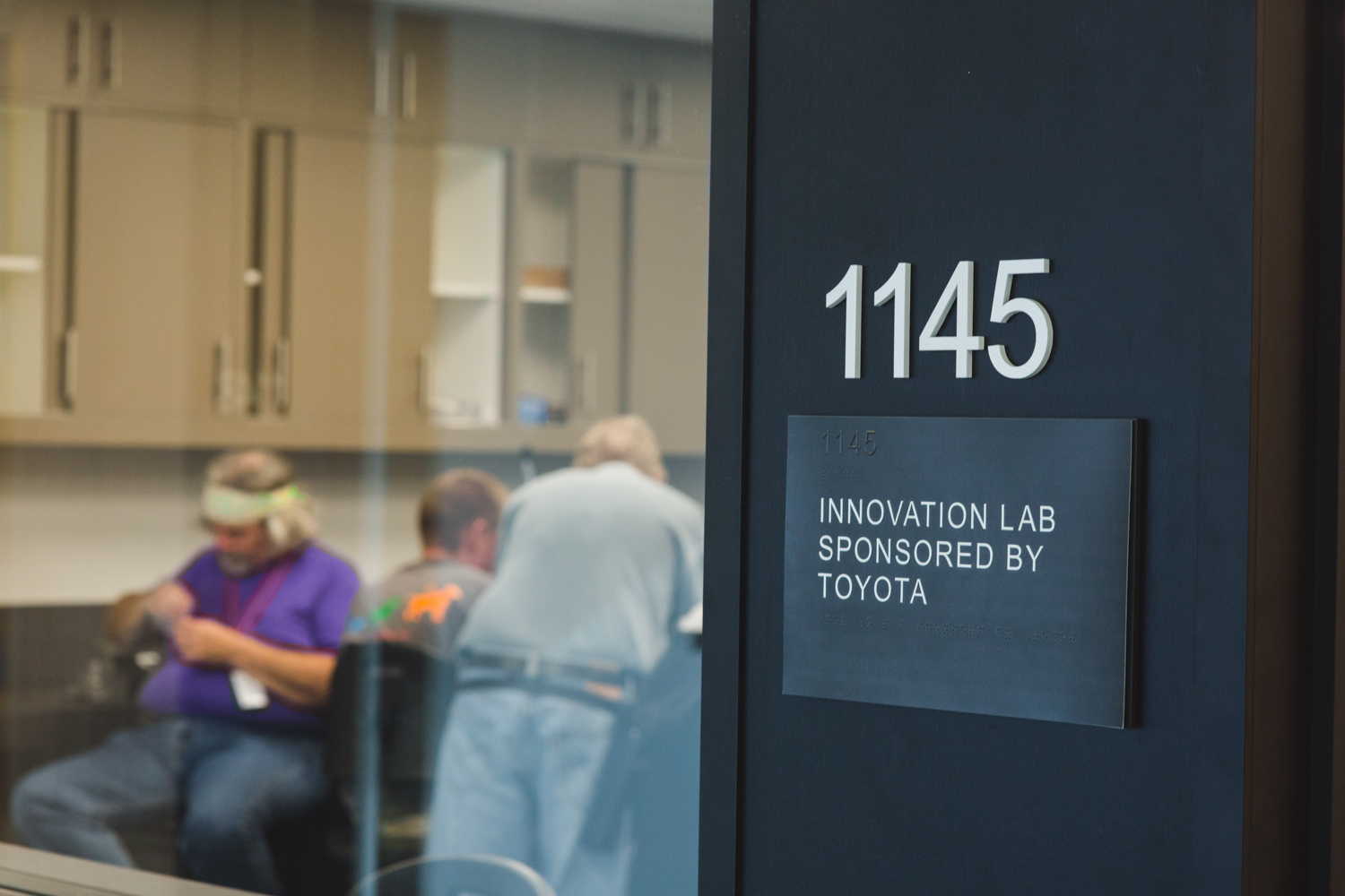 The workshop was held in LightHouse's Innovation Lab on the 11th floor. A close-up of the sign outside the STEM lab in room 1145 reads “Innovation Lab Sponsored by Toyota”. A large window reveals a few students hard at work inside the lab.