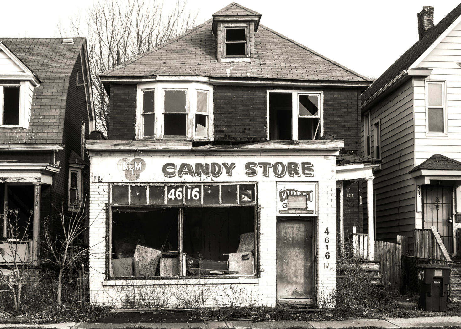 Photograph 3: An old, closed-down, shuttered candy store. A clutter of old boxes and furniture appear through the gaping window. Click the image to hear the corresponding audio file.