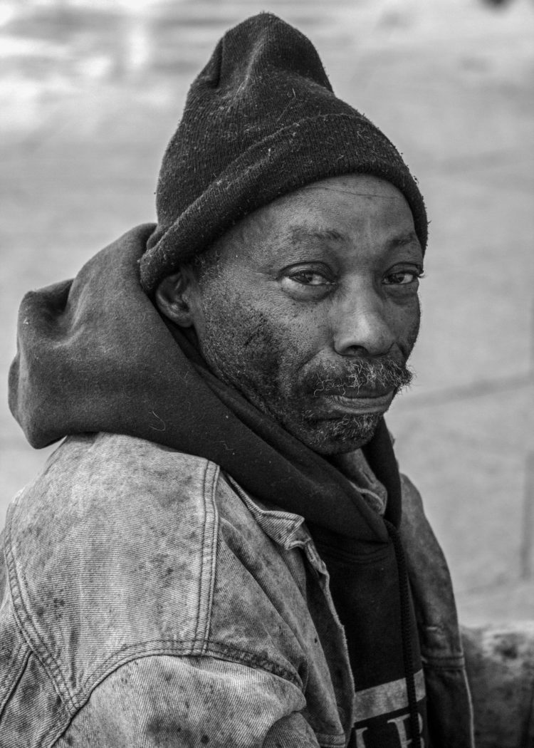 Photograph 4: A man in a knit cap, denim jacket and hoodie looks at the camera with a steady gaze. Click the image to hear the corresponding audio file.