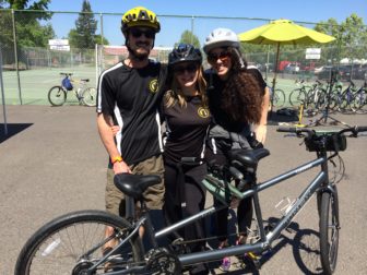 Three friends stand together behind their tandem bike