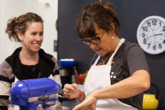 Cooking Instructor Sydney Ferrario and student Jane Flower laugh and bake in the LightHouse Teaching Kitchen.