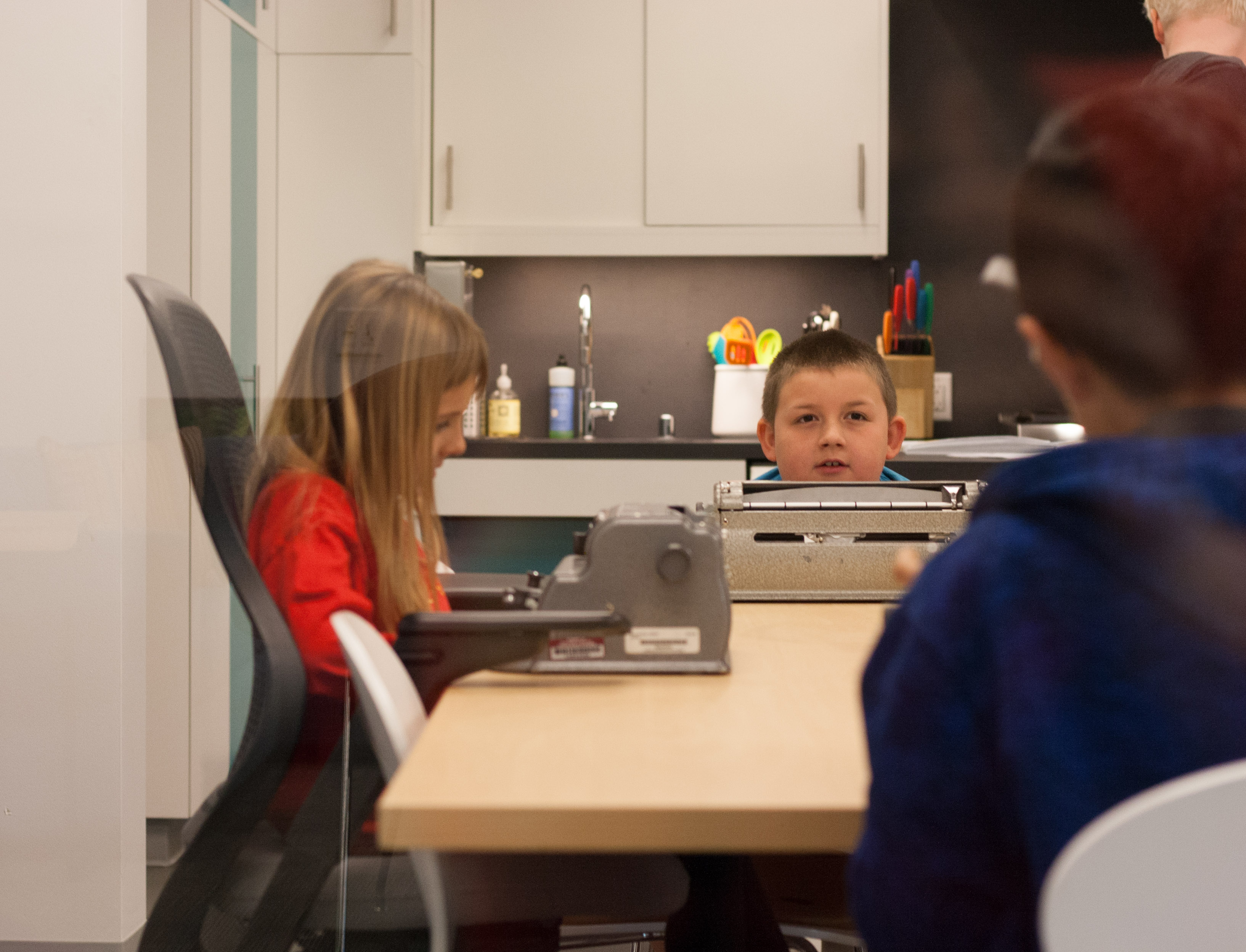 The apprentice sit in front of their braillers in the 11th Floor Kitchen getting ready for testing to start.