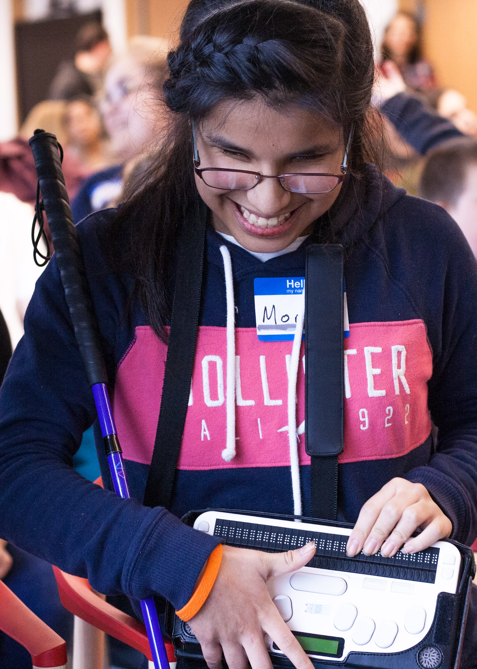 Junior Varsity Competitor Monse smiles while holding her cane and a braille notetaker.