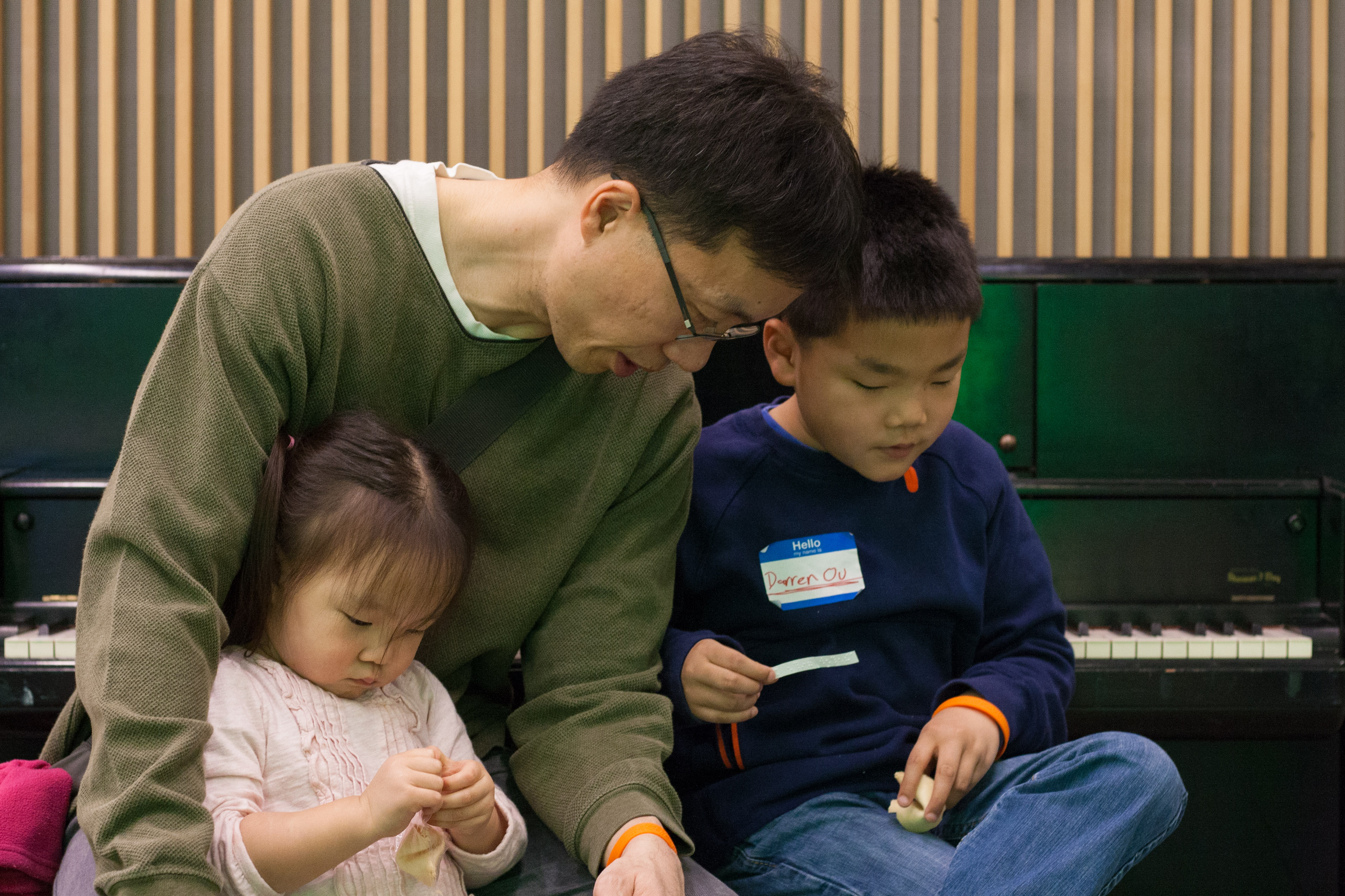 Competitor Darren sits on a piano bench with his dad and little sister reading his braille fortune from a fortune cookie. The message? "Never give up."