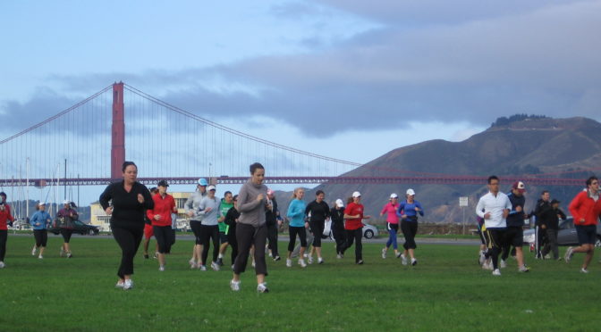 A group of runners take off across a field with the Golden Gate Bridge in the background.