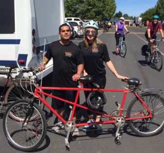 Young woman stands to the left of her tandem partner behind a bright red bike on a bike road.