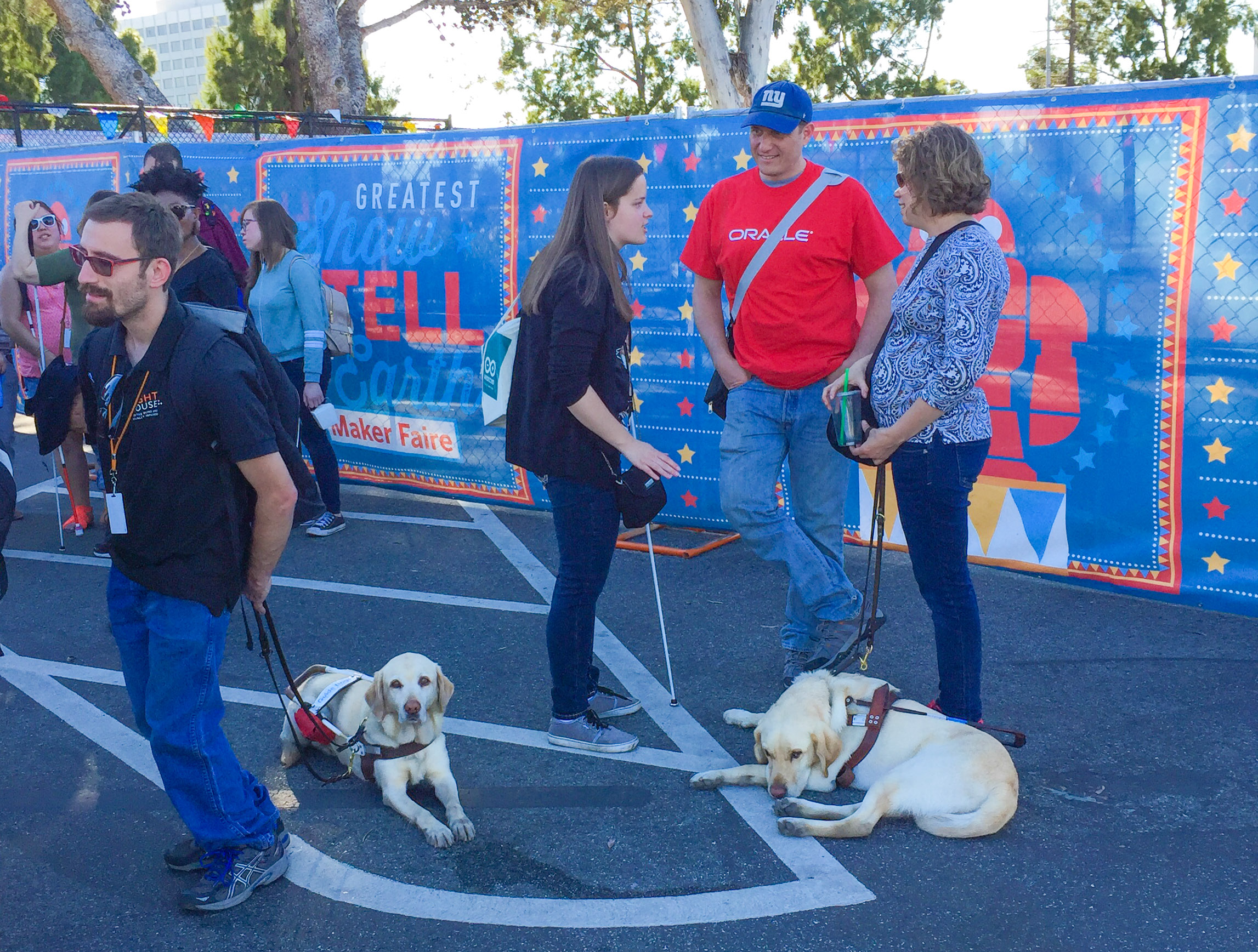 Three participants stand outside of Maker Faire chatting with an Oracle Volunteer.