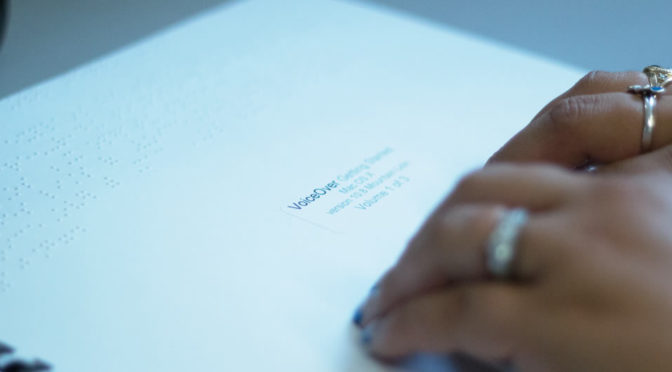 A closeup of a someone's hands as they read a Braille Apple Manual.