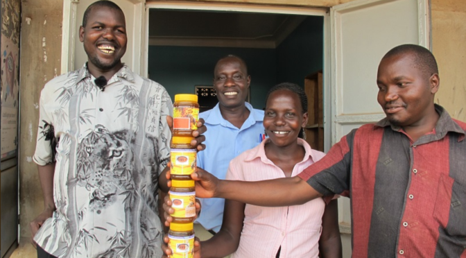 Ojok stands with a group of friends and fellow trainers, holding jars of Hive Uganda honey.
