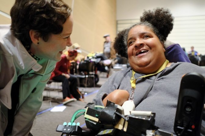 Two women, one standing and one in a wheelchair, laugh and talk at Sunday Superfest screening.