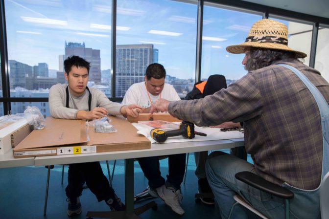 George Wurtzel shows two male students the difference between Phillips-head and slotted head screwdrivers. 