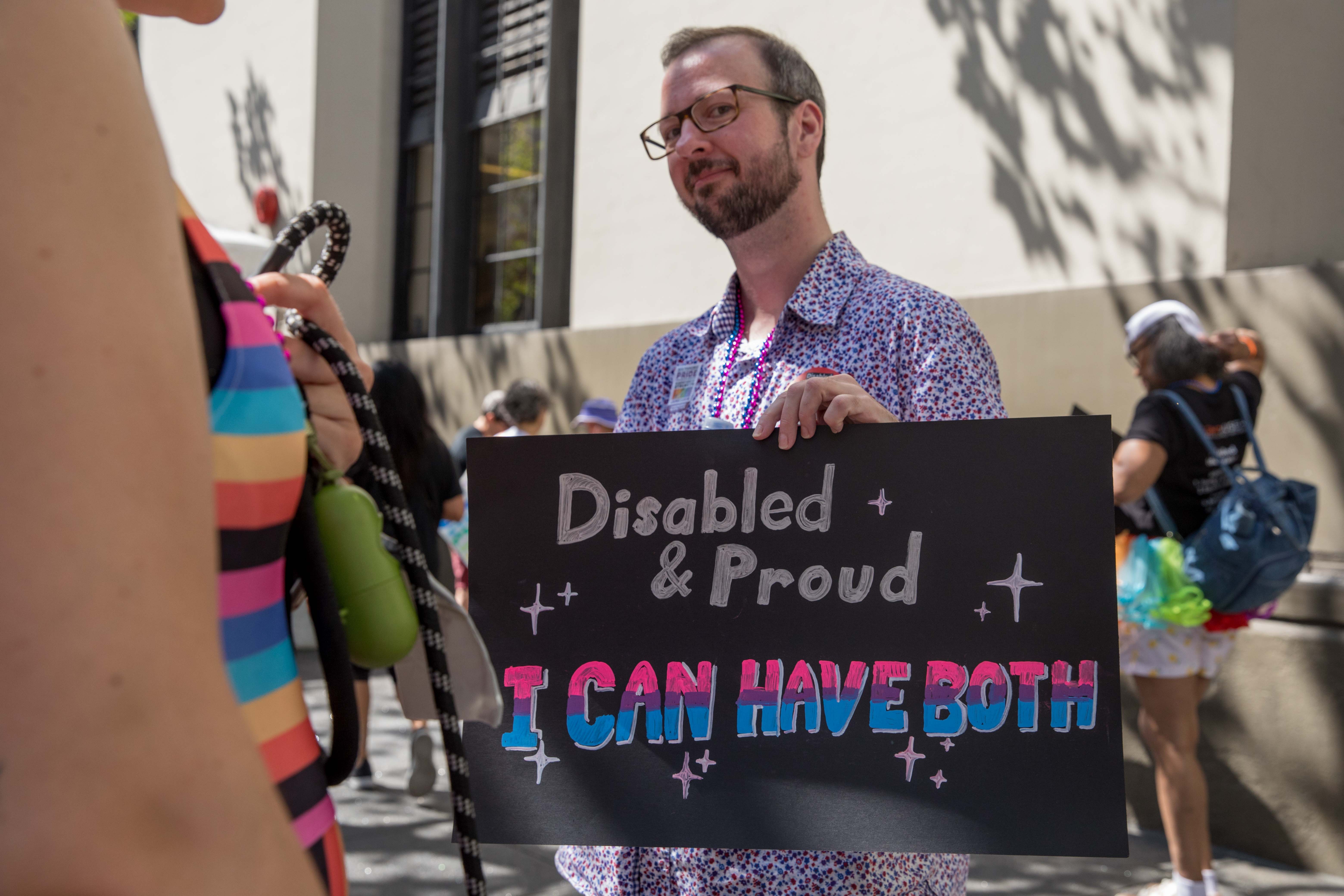 A contingent member from the Mental Health Association of San Francisco smiles and holds a sign that reads, "Disabled & Proud. I can have both."