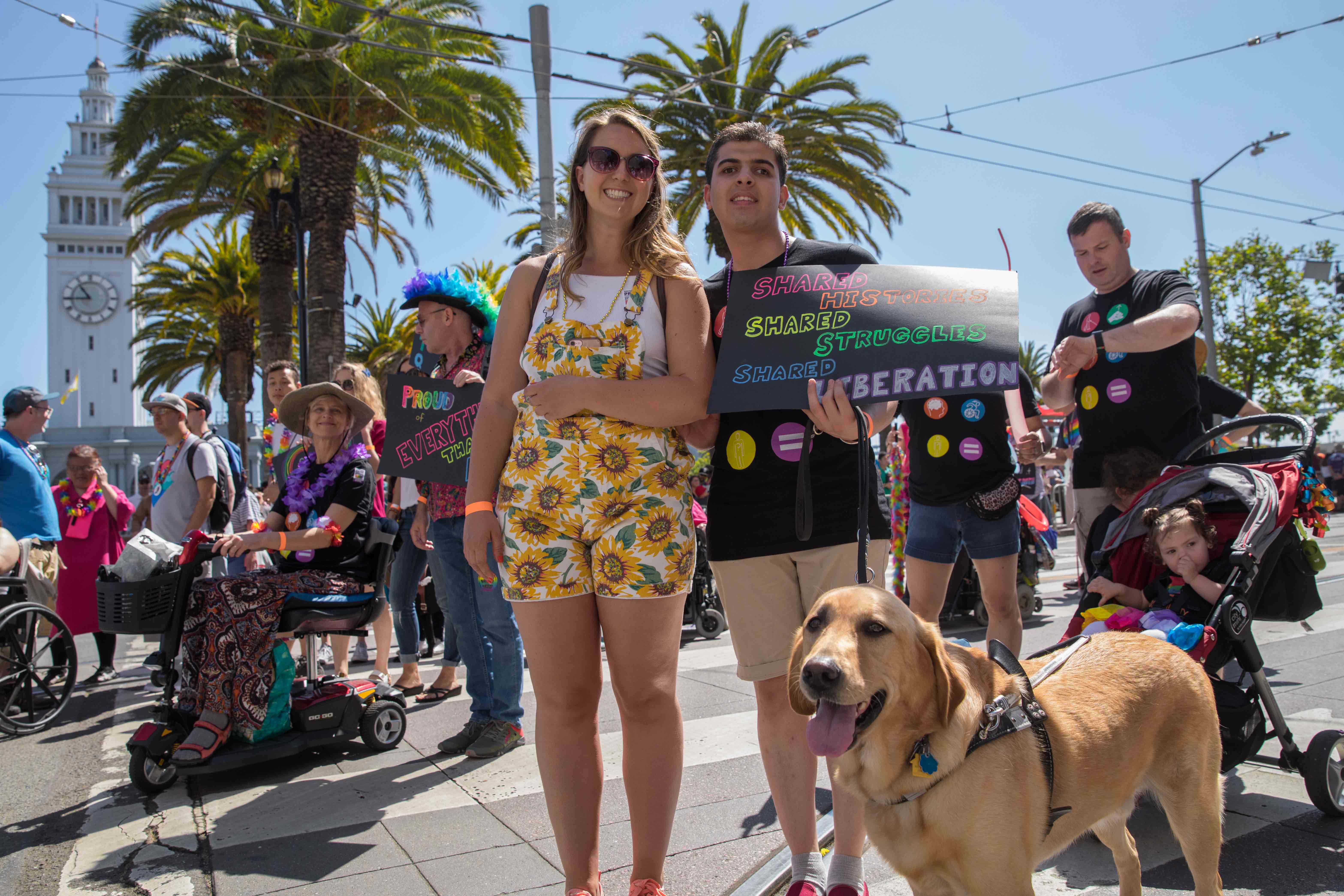 A LightHouse student stands with his guide dog and a volunteer holding a sign that reads, "Shared history, shared struggles, shared liberation".