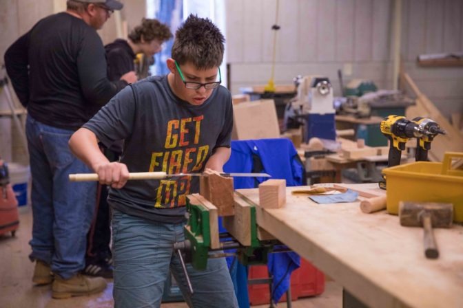 A camper concentrates while using a saw during a woodworking tutorial.