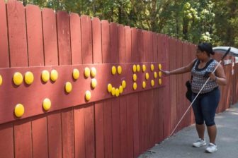 LightHouse Social Media Specialist Christina Daniels looks at a new bright yellow braille sign on the pool fence that reads 'Swimmin' Pool.'