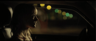 A profile shot of a woman sitting in her car, looking distraught.