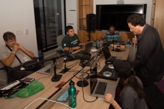 Audio Academy students, instructor Clarence and LightHouse Board member Josh Miele assemble in the Board Room around DJ equipment to listen to music.