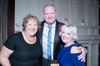 A trio of Gala attendees embrace, smiling for the camera.