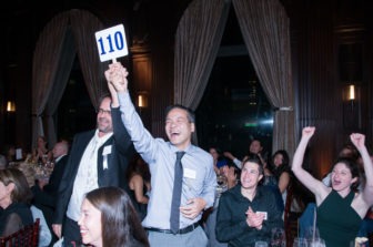 An auction bidder holds up his sign marked "110" with enthusiasm, in a crowd of cheering people.
