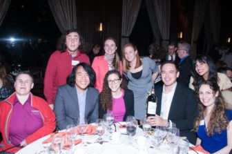 A large group of a dozen Gala attendees pose for a photo - one row sitting at the dinner table, with another row standing behind.