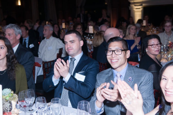 A group of Gala attendees clap, smiling, seated at tables.