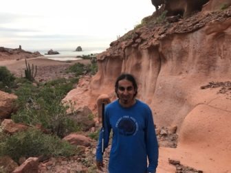 Ahmet Ustunel stands in a park with red rock craters, holding his white cane.