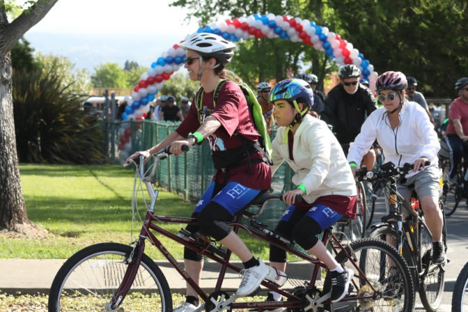 Maycie, a young woman who is blind, rides on a tandem bicycle with a partner, who is a middle aged woman.