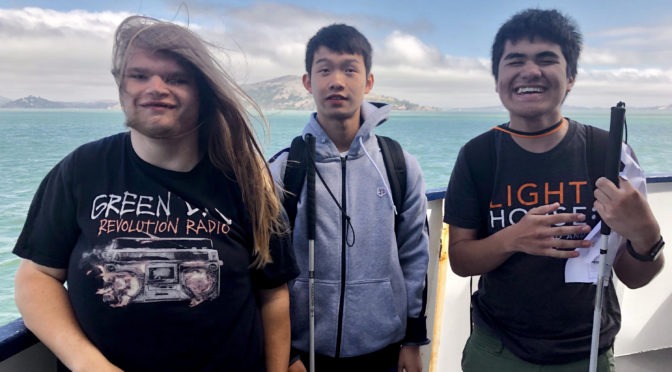 Three Yes Academy Students on a Ferry with their White Canes, looking at the camera and smiling.