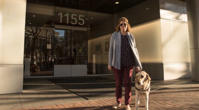 Access Technology director Erin Lauridsen standing outside LightHouse headquarters with her guide dog Kendall