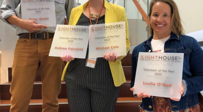 2022 Volunteers of the Year, Leslie O’Neil and Peter Goetz, stand on the LightHouse staircase with Allyson Ferrari, Volunteer Manager. Leslie and Peter are holding their Volunteer of the Year plaques. Note: Masks were temporarily removed to take this photo