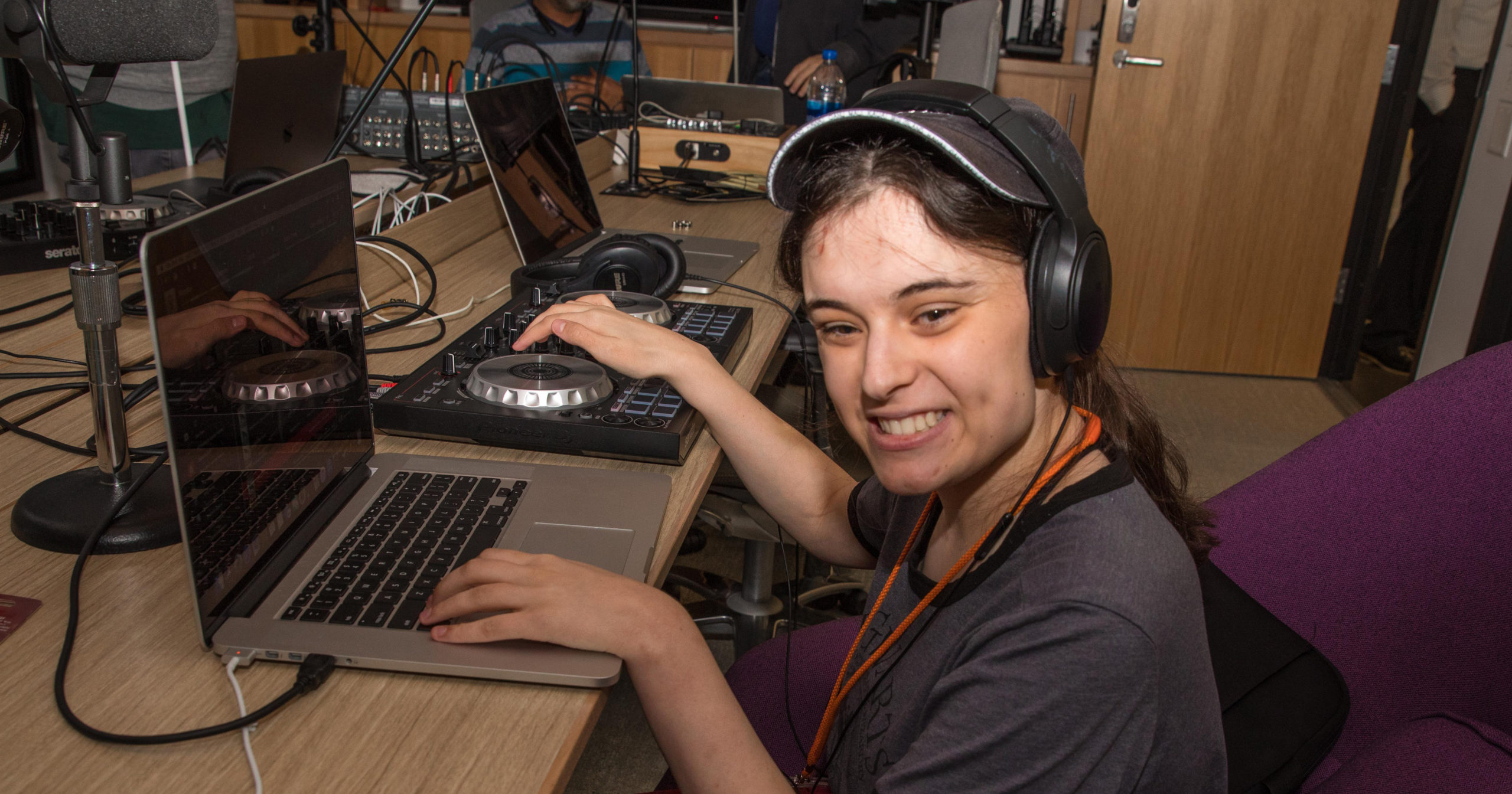 A student wearing headphones smiles as they use audio mixing equipment connected to a lap. 
