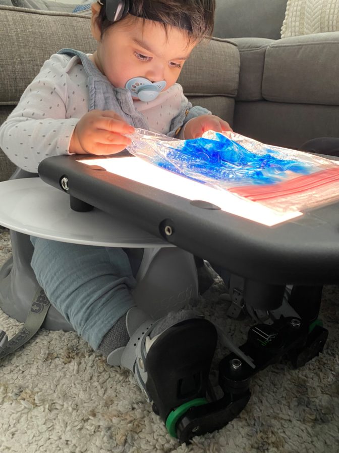 Little Learner with a pacifier in his mouth plays with a translucent blue material on a lightboard