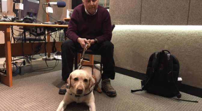 Stephen Kuusisto, blind poet and the first guest speaker in the Writers Workshop, sits at a desk with his guide dog