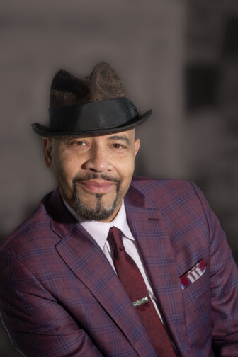 William Rhodes wearing a burgundy and purple plaid suit and a hat.