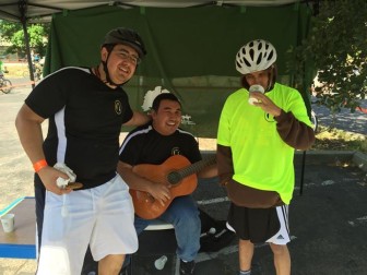 Anthony Dalli, Jimmy Cong and Andy Rodriquez stand in front of the Enchanted Hills Camp banner. Jimmy is in the center playing gum gum style on the guitar