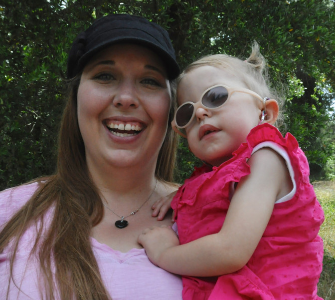 baby rests in mother's arms, sporting white-rimmed sunglasses