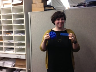 Naomi Rosenberg stands holding a 3D printed cross-section of a worm and a set of symbols used in 3D printed maps