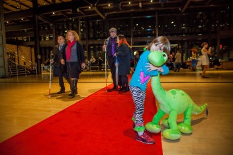 a little girl hugs a dinosaur plush doll next to the red carpet