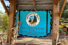 The Enchanted Hills Camp​ sign on a cyan-blue background.