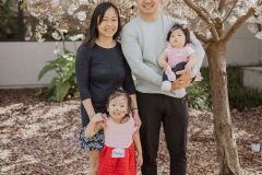 A family of four poses together - Dad is holding Little Learner and Mom holds older sibling's hand