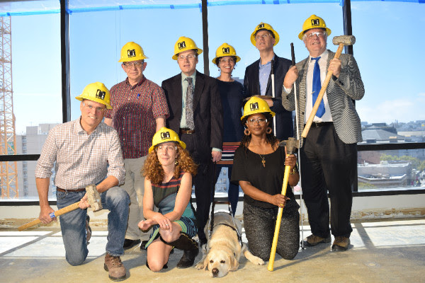 LightHouse Board and Staff, some with white canes or dog guides, pose with hardhats and hammers inside the new LightHouse.