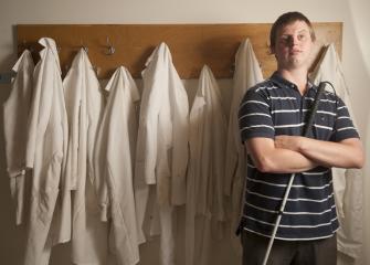 Hoby Wedler stands, arms crossed, in front of lab coast hanging on hooks